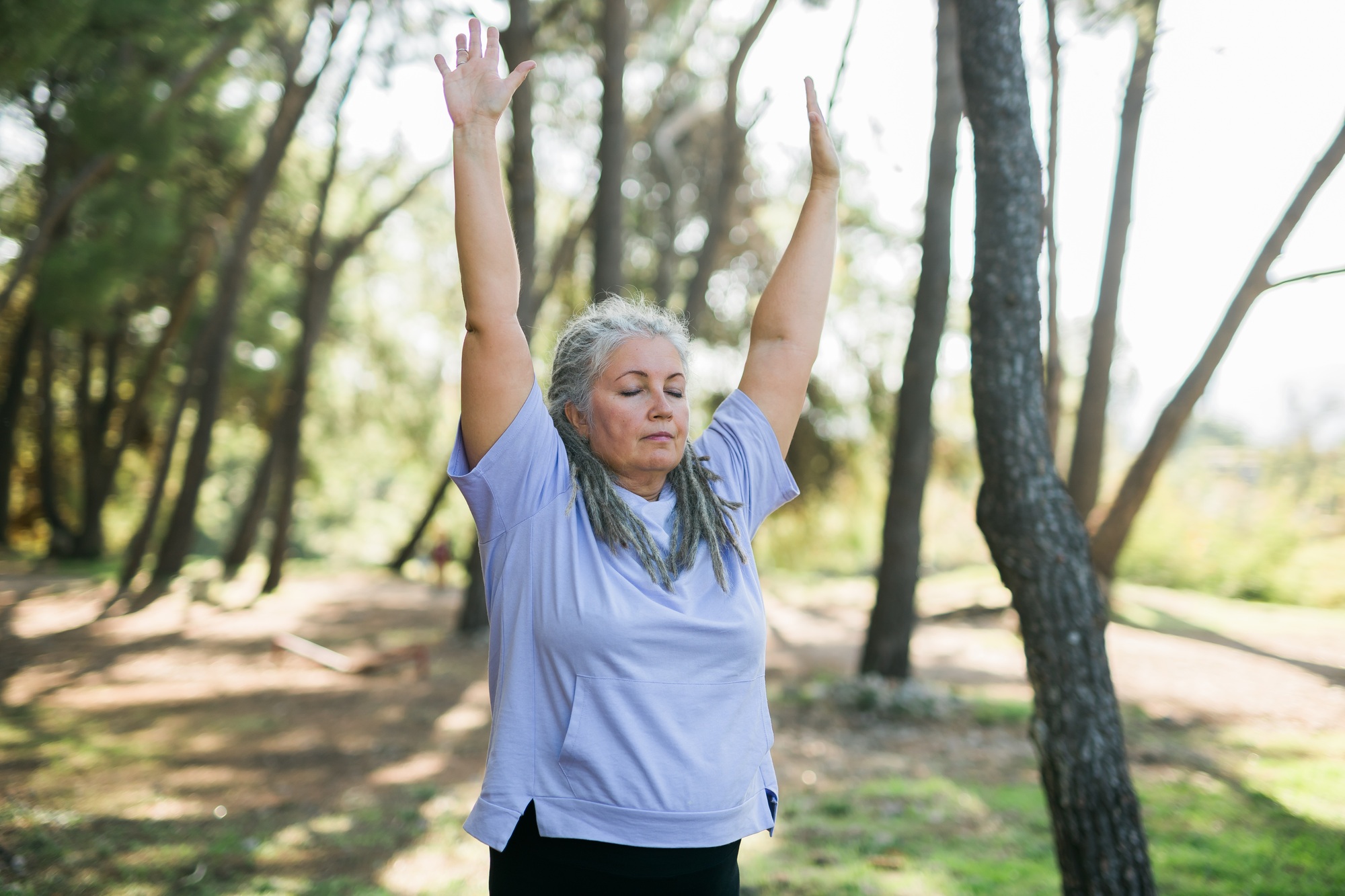 Mature old woman with dreadlocks practicing yoga and tai chi outdoors - wellbeing and wellness